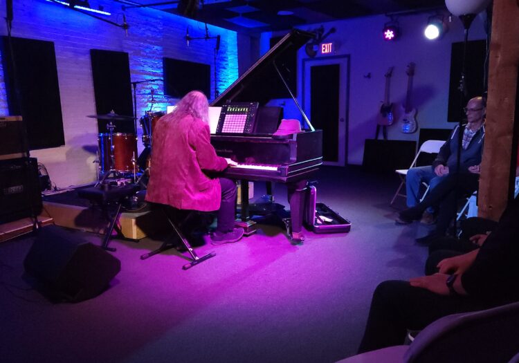A piano player playing on our in house Mason & Hamlin Baby Grand with our blue and magenta stage lighting
